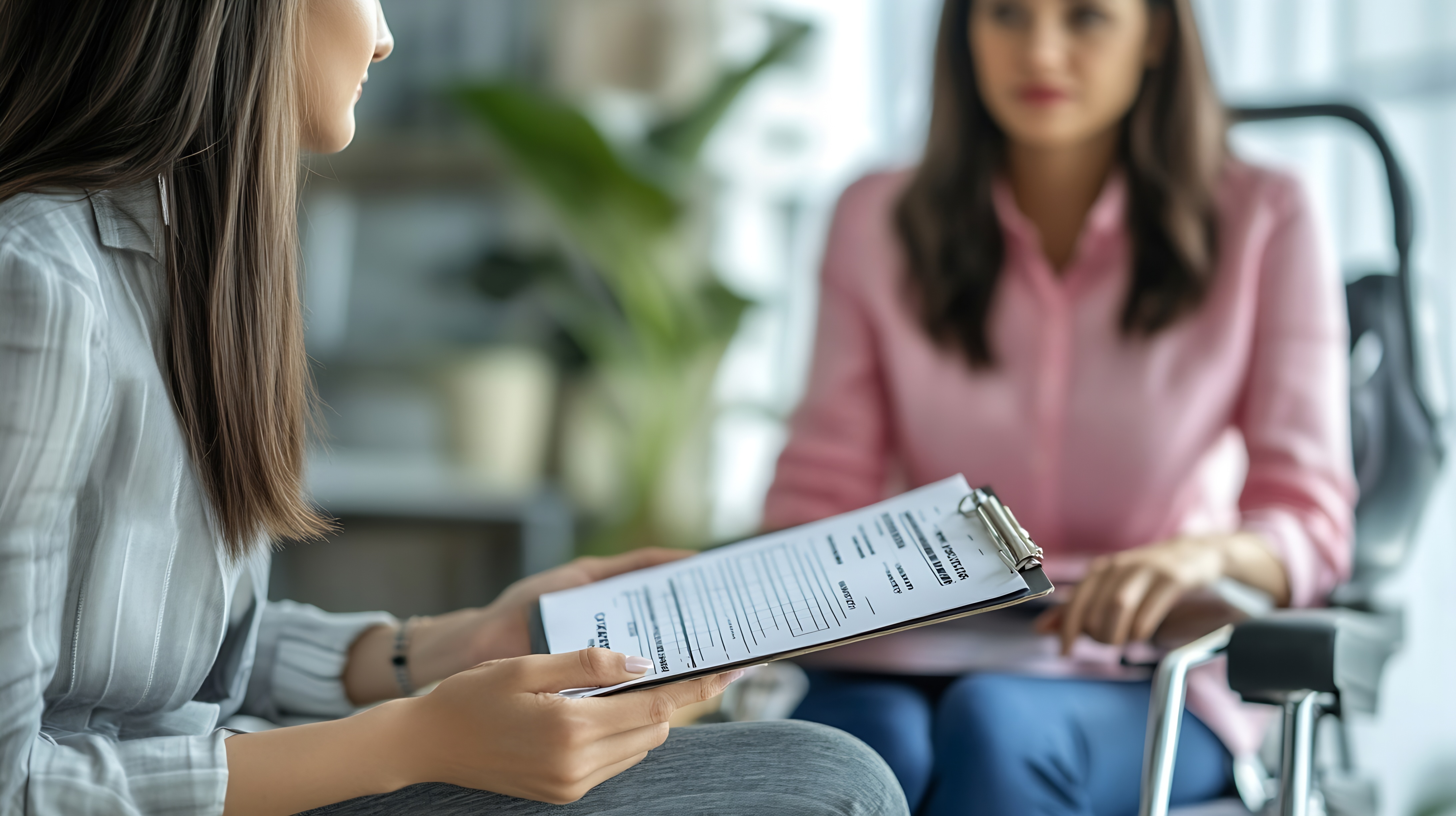 A professional holding a clipboard with a form while having a discussion about disability insurance for physicians with a woman sitting in a wheelchair.